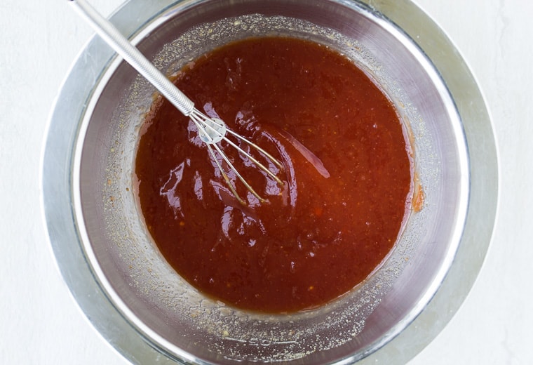 Barbecue sauce in a silver bowl with a small whisk over a white background