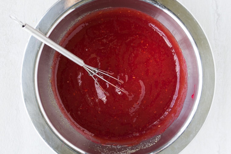 Raspberry Barbecue Sauce in a silver bowl with a whisk over a white background