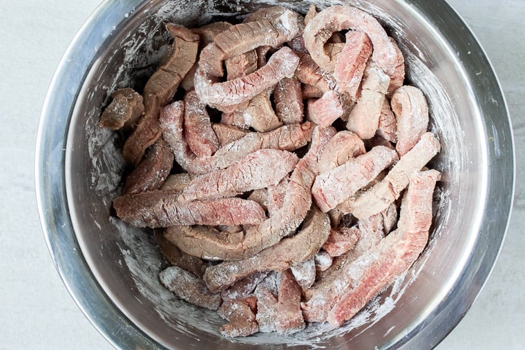 Beef strips tossed with cornstarch in a silver bowl