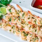 Sweet Chili Lime Grilled Shrimp on a white servign tray with lime, cilantro, and a dish of sweet chili sauce on the side