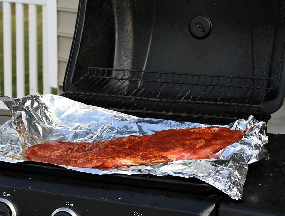 A rack of ribs on a piece of foil cooking on a grill