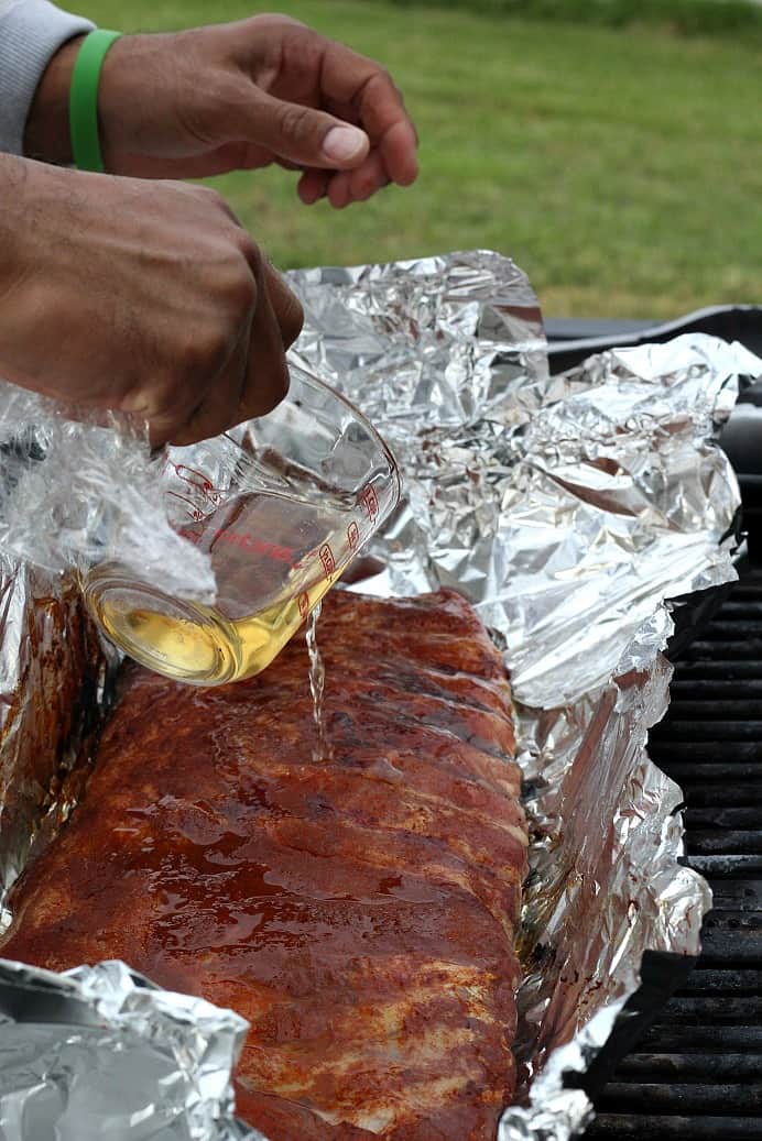 Apple Cider Vinegar being poured onto a rack of ribs on a piece of foil