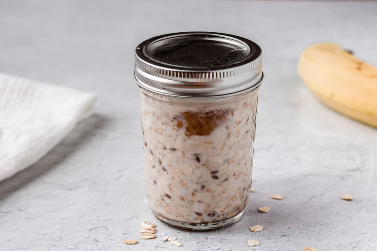 Peanut butter oats in a mason jar with the lid in and a banana in the background