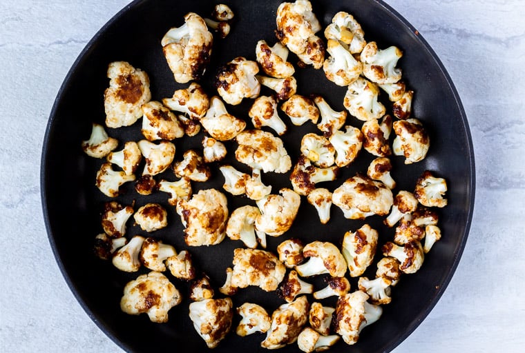 Cauliflower florets cooking in a black skillet over a white background