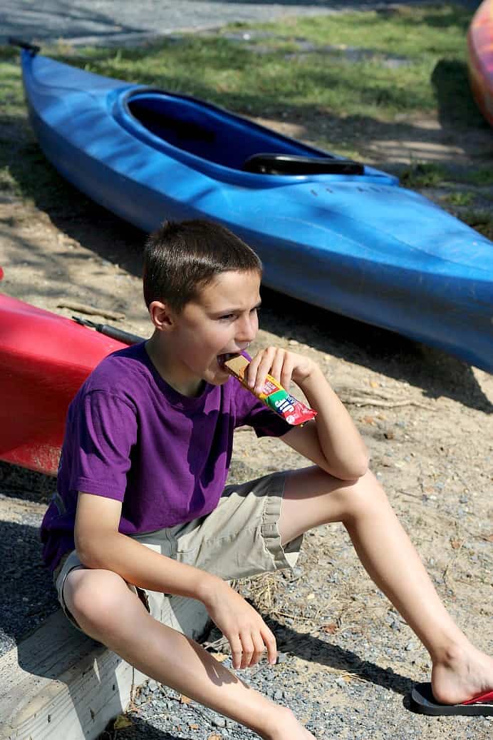 Child Eating a Granola Bar Near Boats