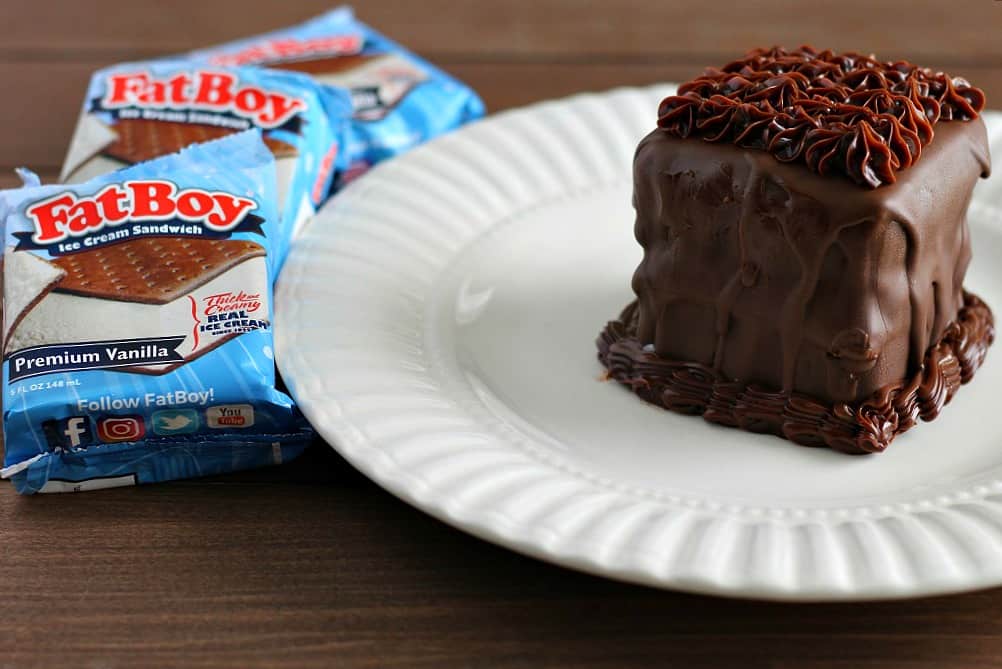 a finished Ice Cream Sandwich Cake on a white plate on a wood table with 3 fatboy ice cream sandwiches next to it