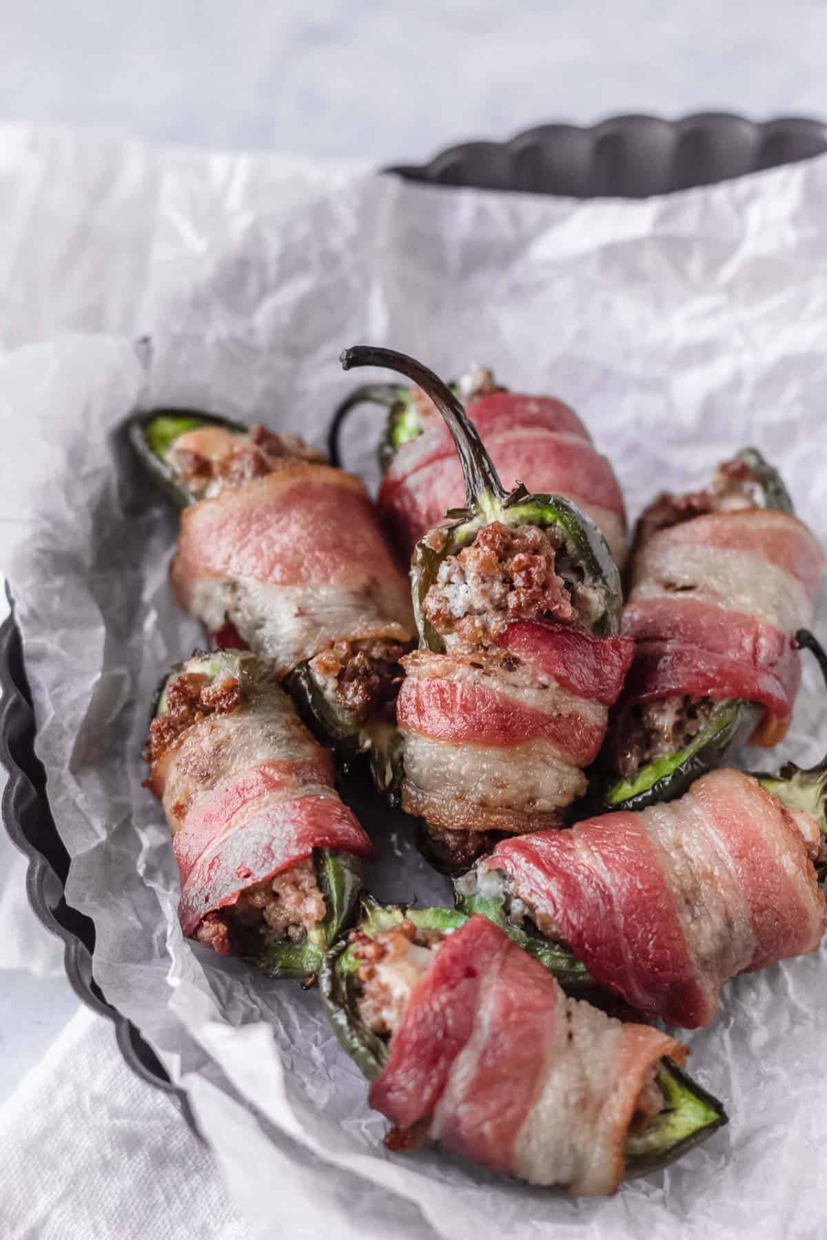 A dark tray lined with white paper and filled with bacon and blue cheese jalapeno poppers