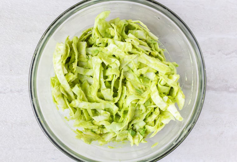 avocado cabbage slaw in a glass bowl over a white background