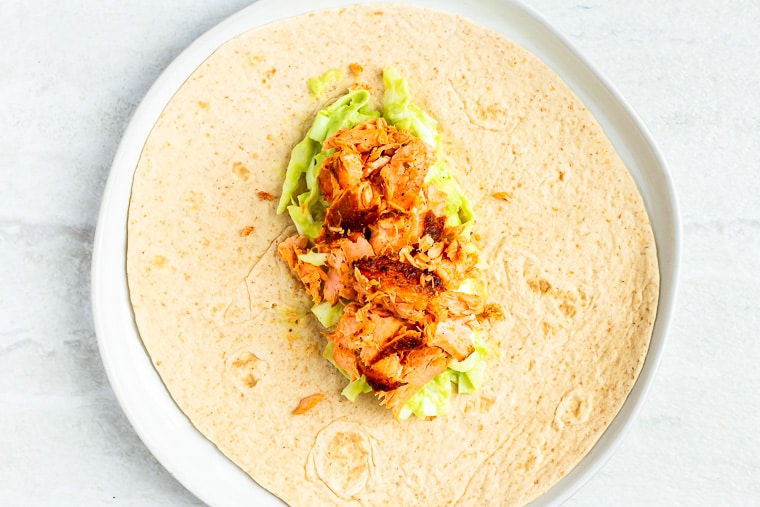 Avocado slaw topped with flaked blackened salmon in the center of a flour tortilla