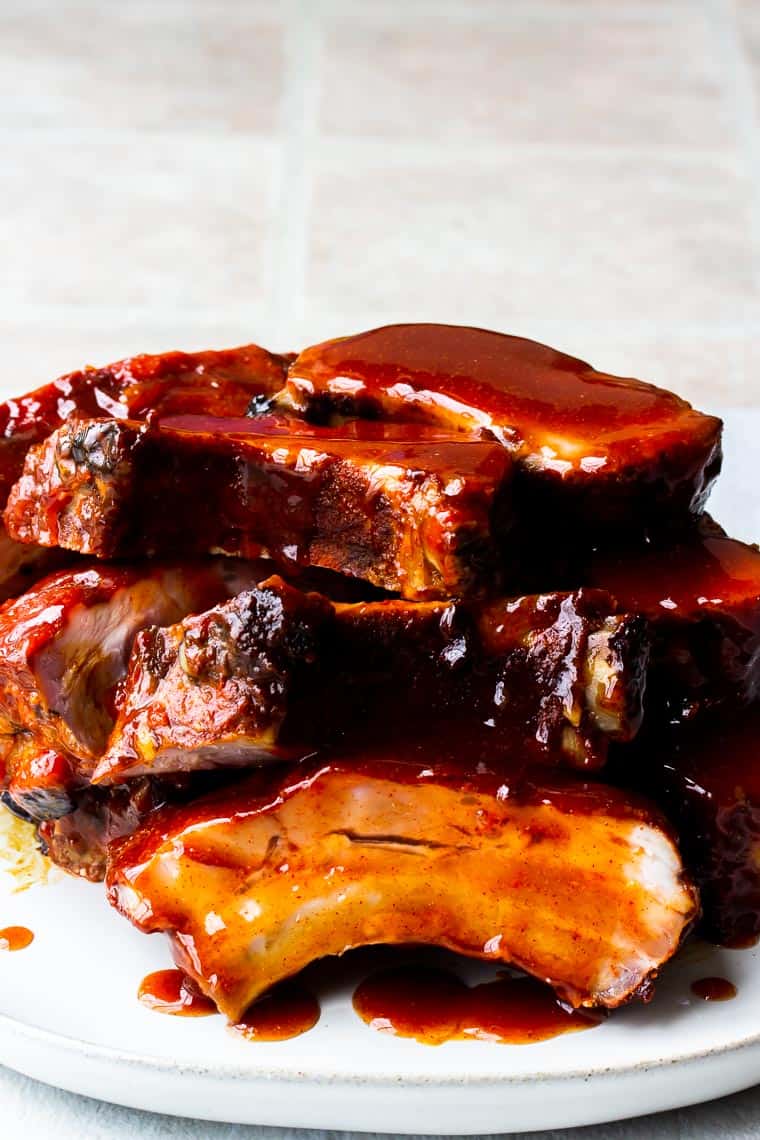 A stack of baby back chipotle honey-barbecue ribs on a white plate with a white background