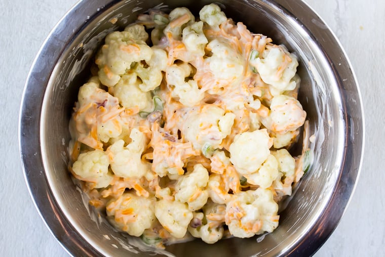 Cauliflower and dressing tossed together in a silver bowl over a white background