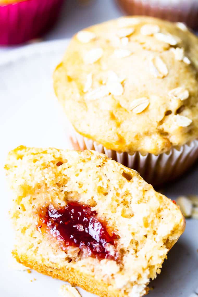 Close up of half a peanut butter muffin showing the jelly inside with a whole muffin right behind it