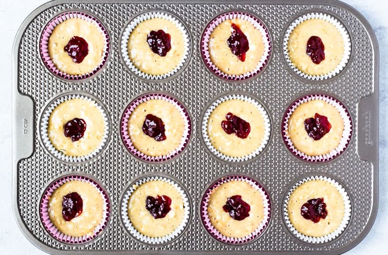 Muffin batter in a muffin tin with a dollop of jelly on top of each one