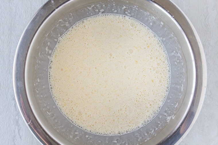 Wet ingredients whisked together in a silver bowl over a white backdop