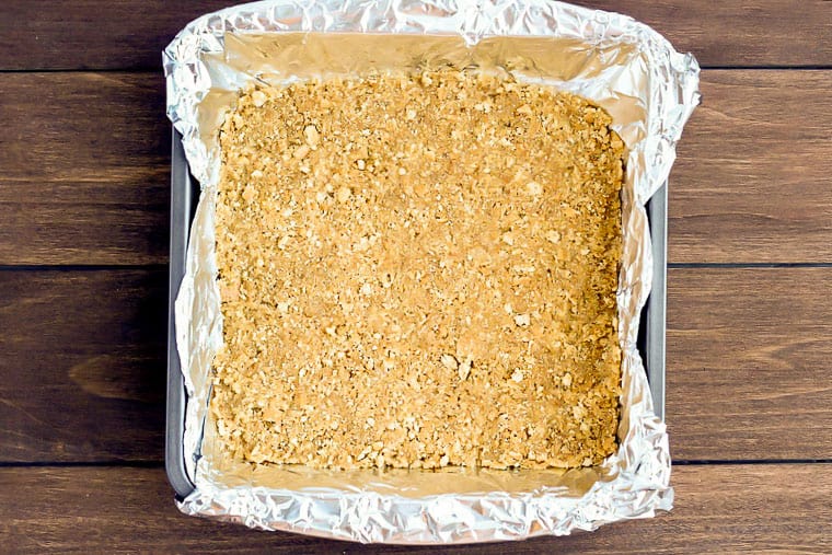 Homemade Graham Cracker Crust in a square baking pan lined with aluminum foil over a wood background
