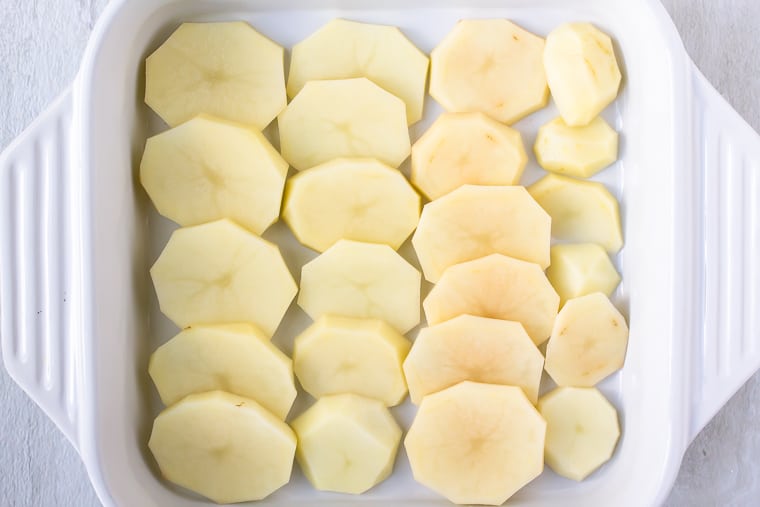 Layer of potato slices in a white, square casserole dish