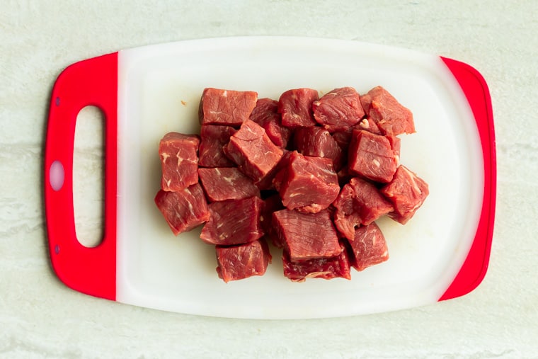 Beef cubes on a red and white cutting board