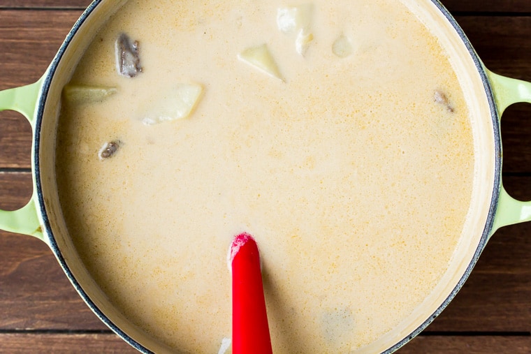 Creamy soup with pieces of steak and potatoes in a cream color Dutch oven on a wood background 