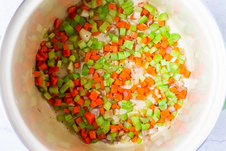 Chopped vegetables cooking in a cream colored stock pot over a white background