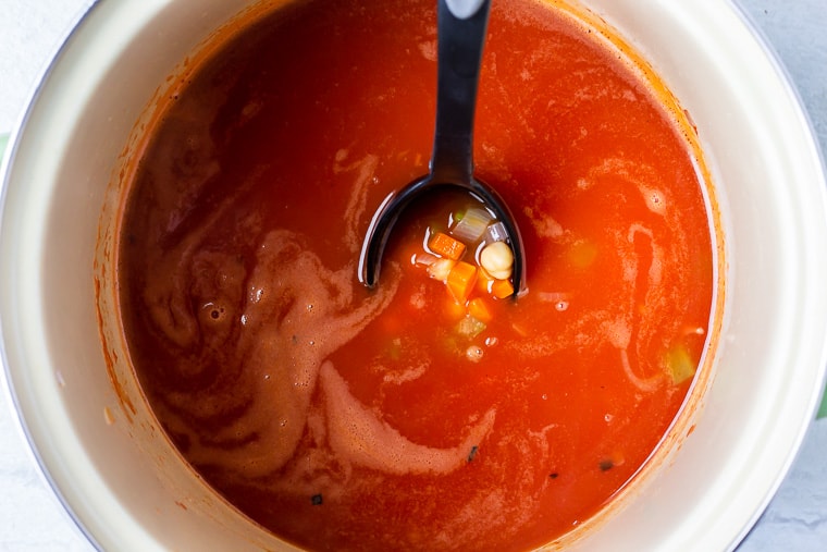 Vegetables and beans in a tomato broth being scooped up with a black spoon