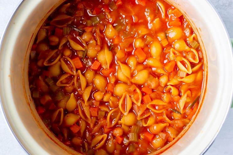 Pasta and beans in a tomato broth in a stockpot over a white background