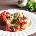 Three Cheese Stuffed Shells with Meatballs on a white plate with garlic and parsley in the background