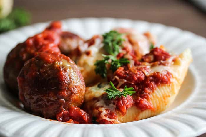 Three Cheese Stuffed Shells with Meatballs on a white plate over a wood background