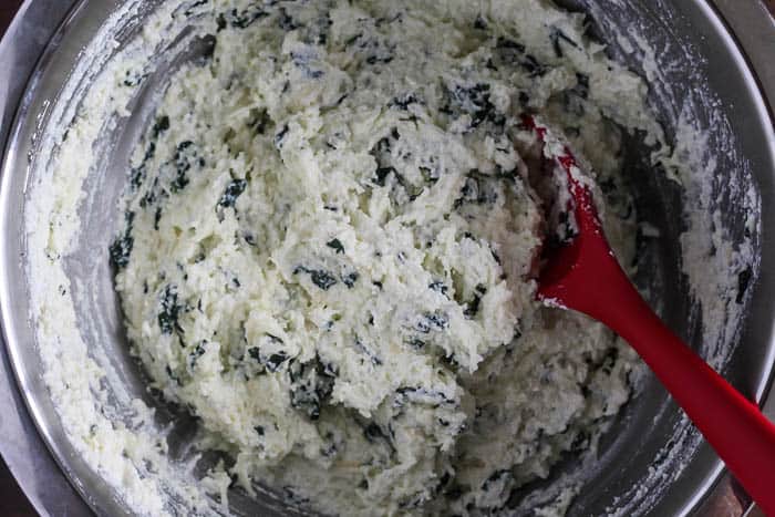 Cheese and spinach mixed together in a silver bowl with a red spoon