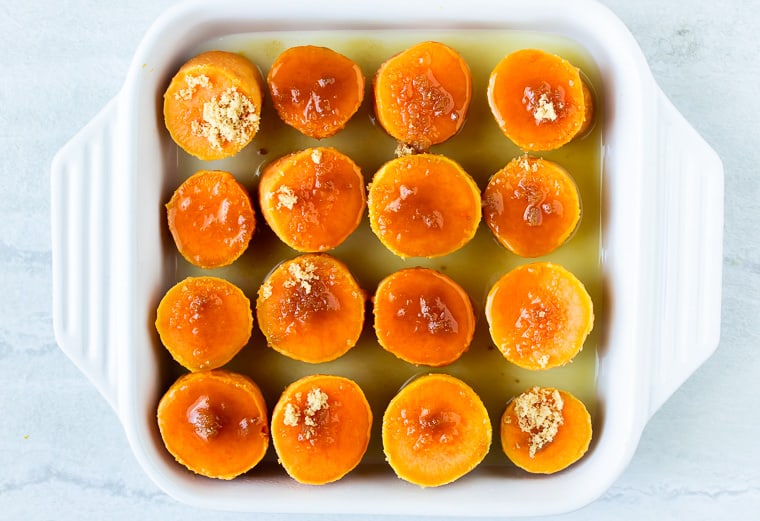 Slices of sweet potatoes with pineapple juice and brown sugar in a white, square casserole dish