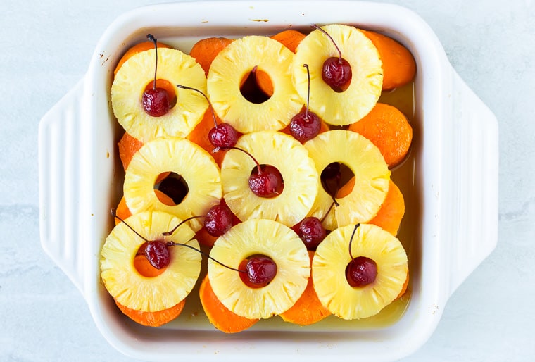 Baked Candied Sweet Potatoes topped with pineapple slices and maraschino cherries in a white, square casserole dish