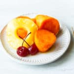 Candied Sweet Potatoes with Pineapple Slices and Cherries on a small white plate on a white background