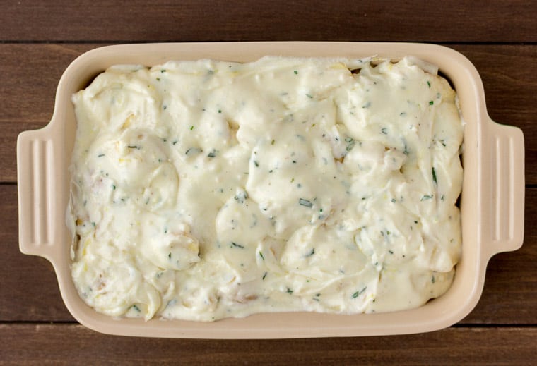 Rosemary Lemon Cream Sauce Over Potatoes in a Baking Dish over a wood background
