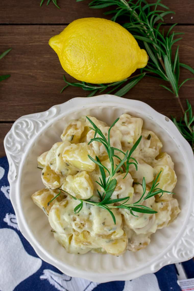 Creamy Rosemary Lemon Potatoes in a White, Round Bowl with a Blue and White Napkin, a Lemon, and Fresh Rosemary on a Wood Backdrop