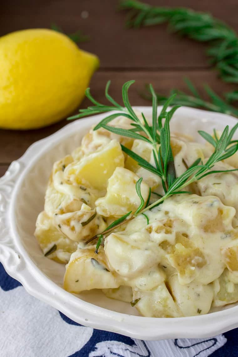 Creamy Rosemary Lemon Potatoes in a White Bowl with Fresh Rosemary and Lemon on a wood background