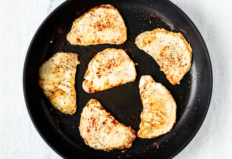 6 pork chops cooked in a black skillet over a white background