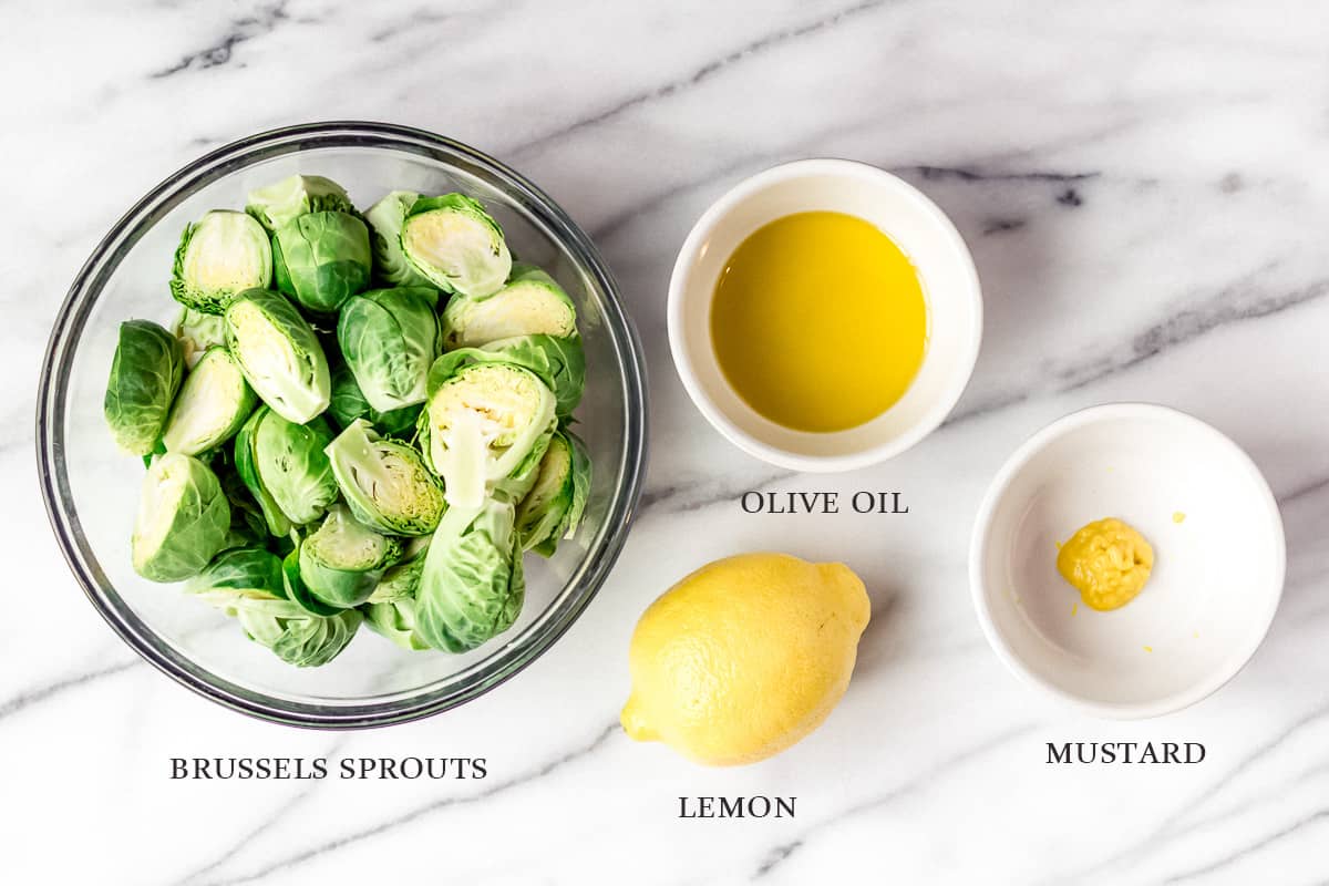 Ingredients to make roasted brussels sprouts and mustard dressing on a marble background with labels