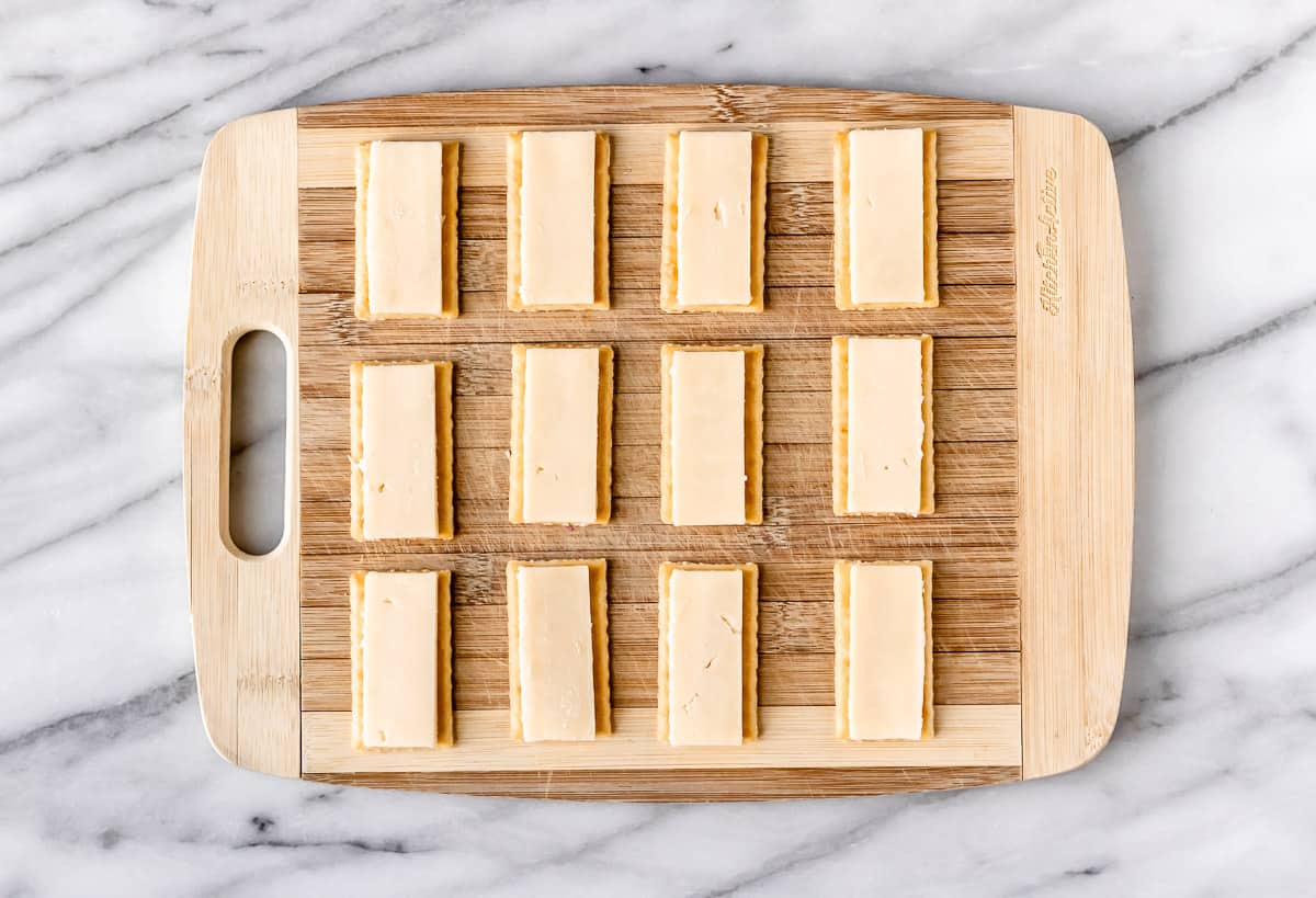 Crackers on a cutting board topped with slices of cheese.