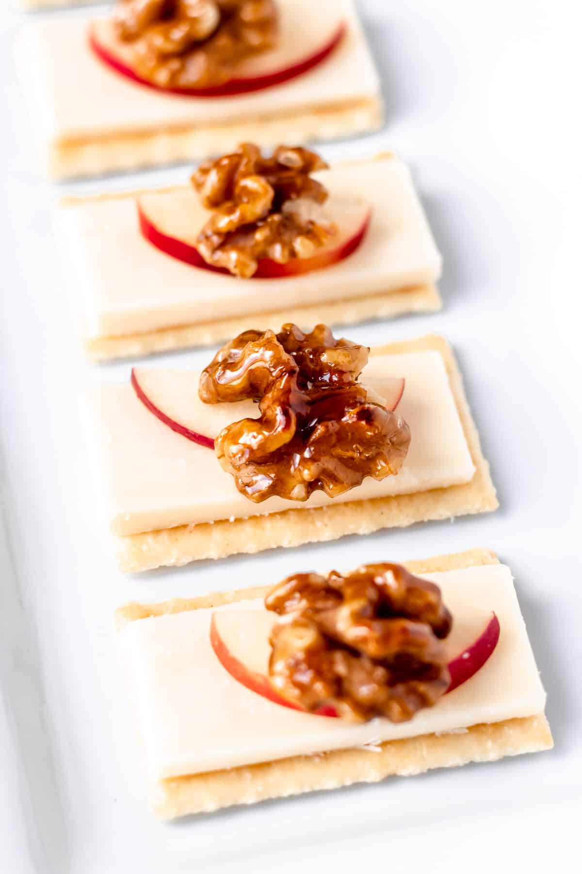 4 cheese crackers with apples and honey walnuts on a white tray.