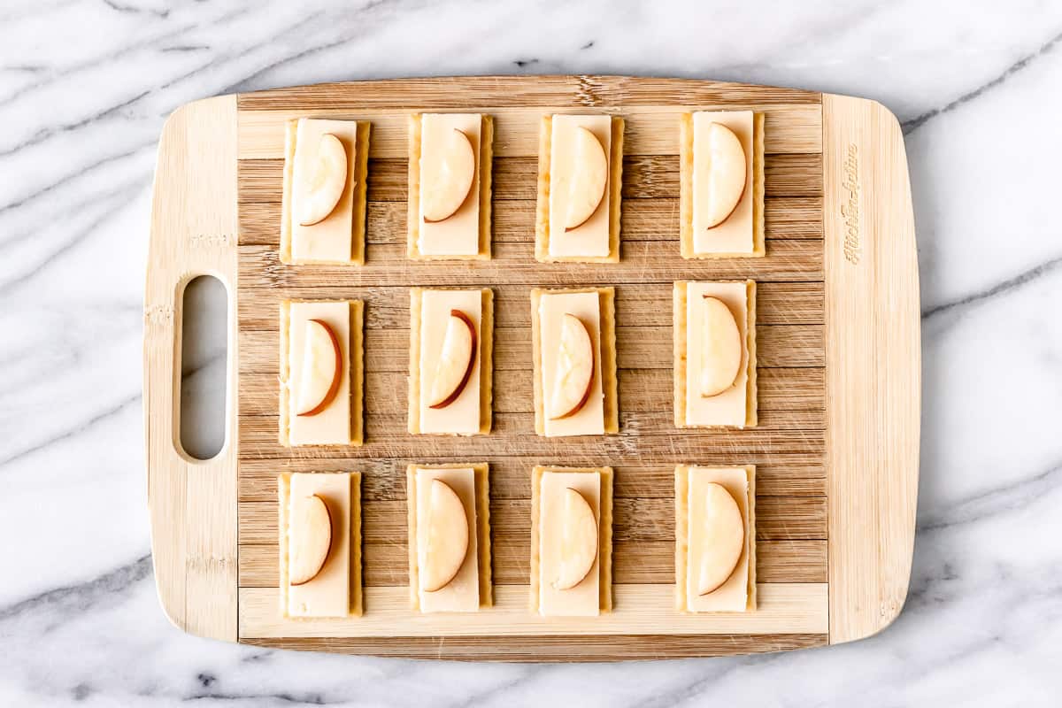 Crackers on a cutting board topped with cheese and apple slices.