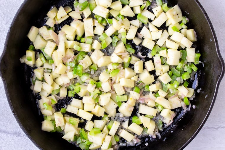 Apples, shallots, and celery cooking in a cast iron skillet