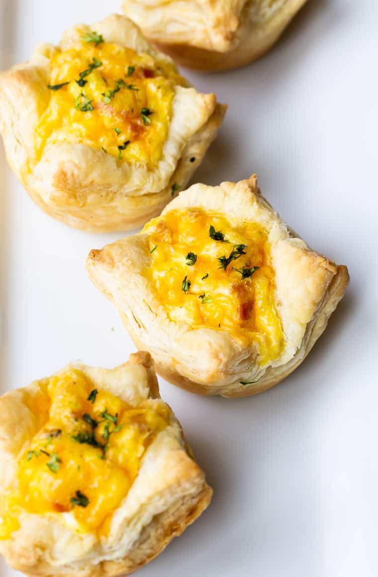 4 Bacon, Egg, and Cheese Puff Pastry Cups close up on a white serving tray