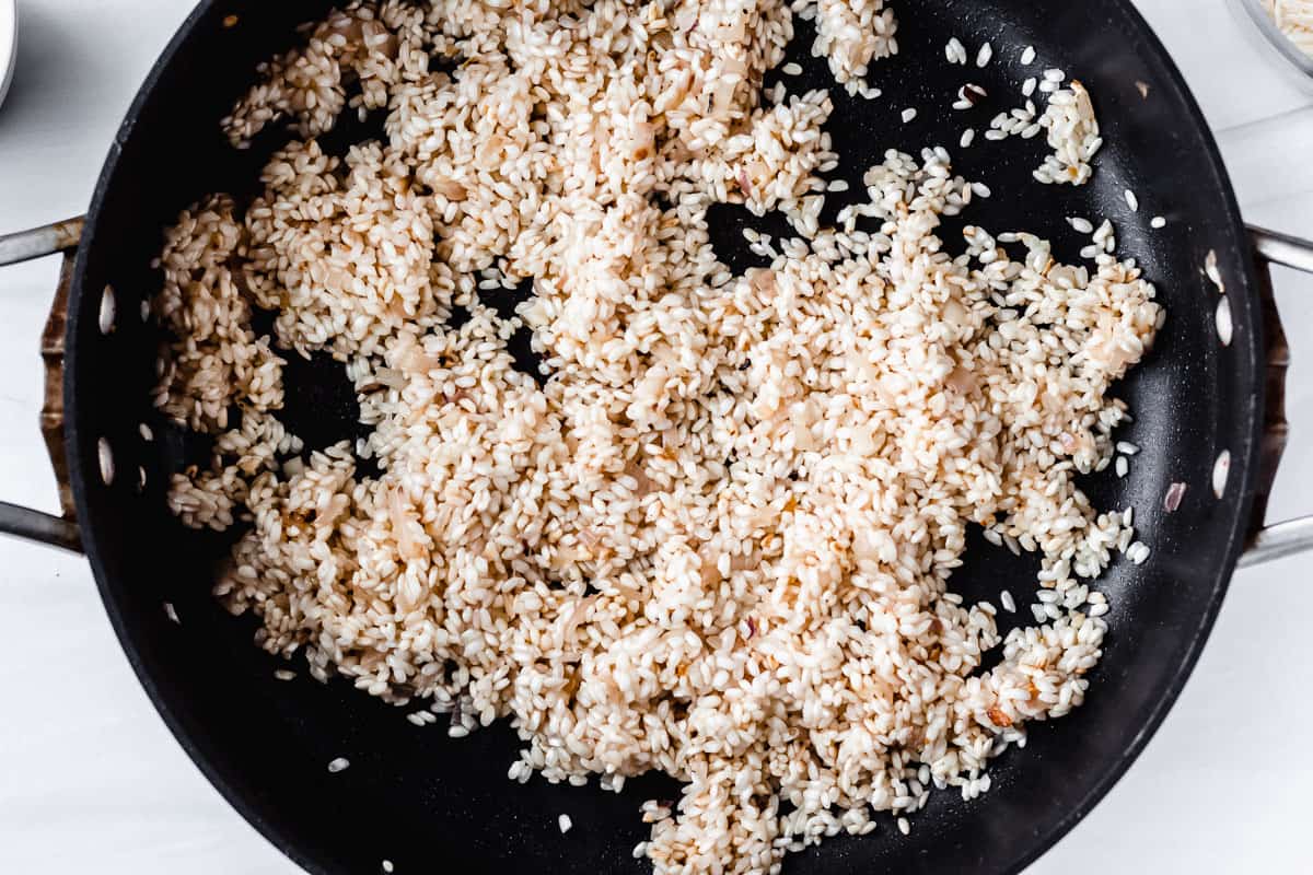 Arborio rice in a skillet with shallots, garlic and wine