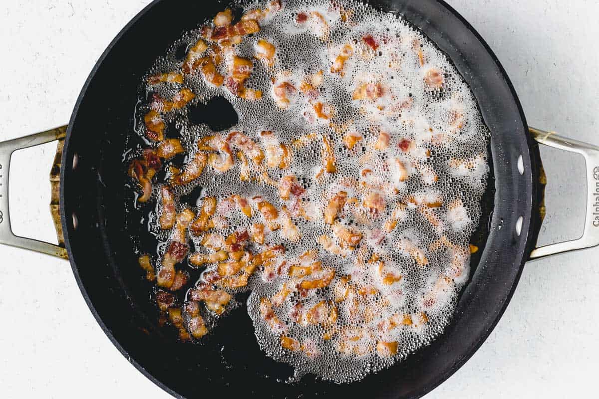 Diced bacon cooking in a skillet over a white background