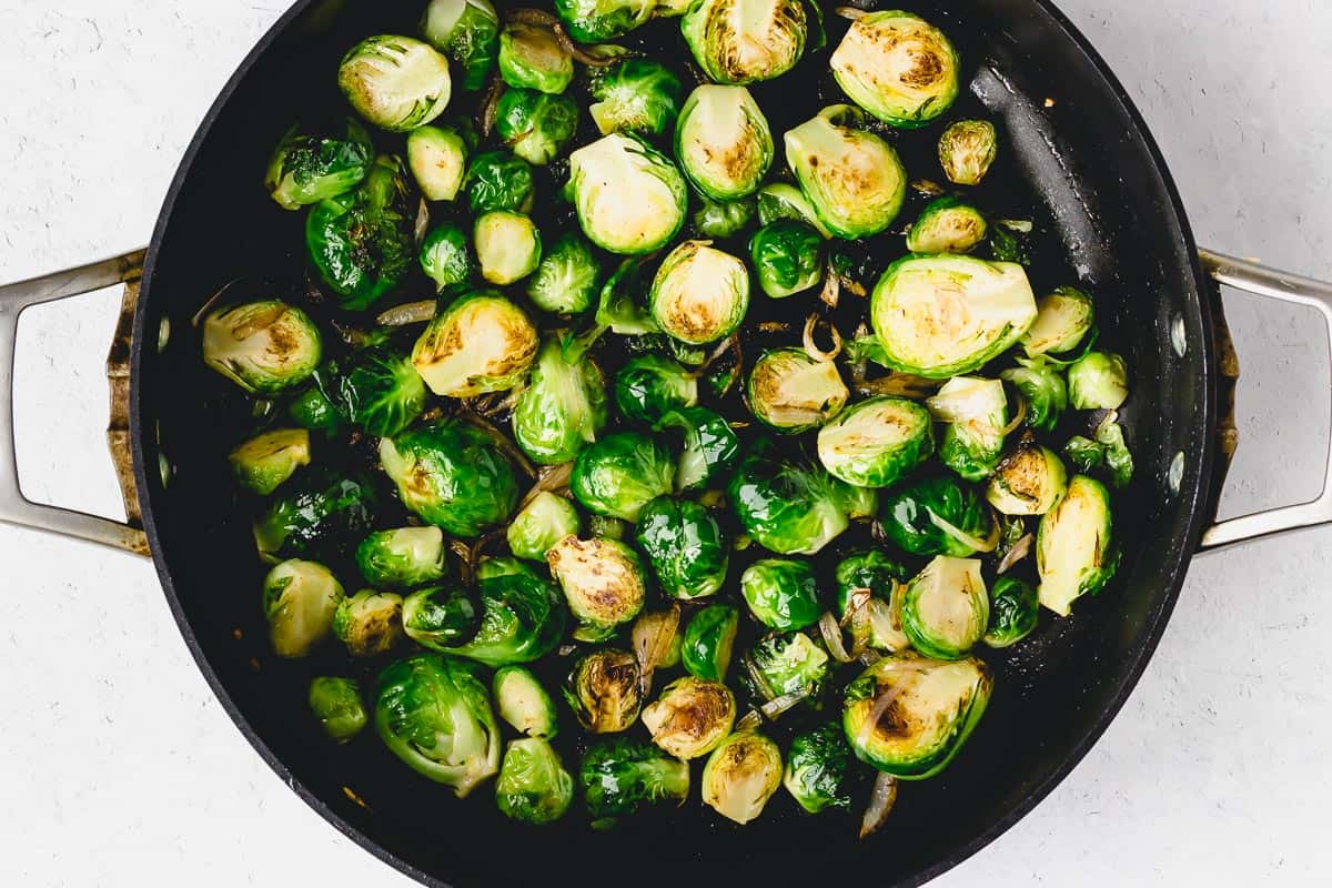 Brussels sprouts cooking in bacon grease in a black skillet