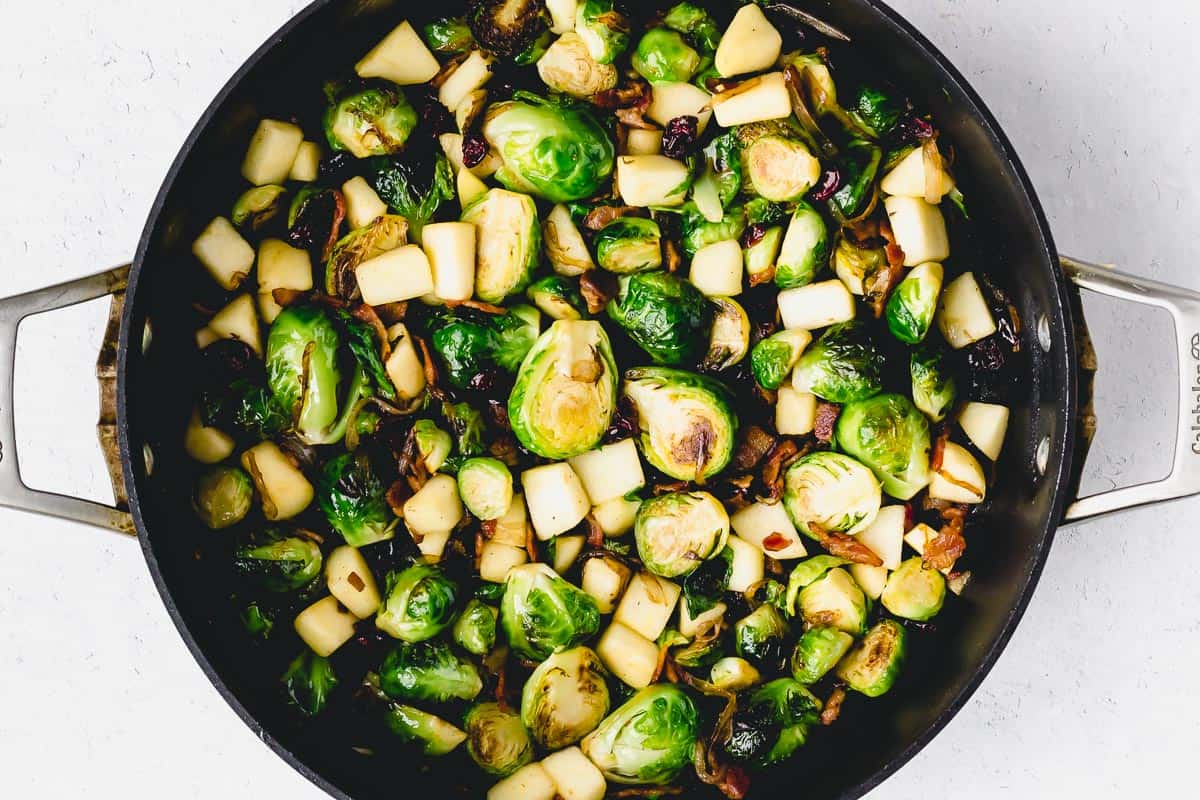 Brussels sprouts with bacon, apples, and cranberries cooking in a black skillet
