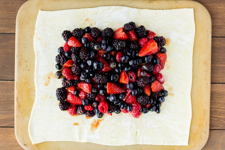 Mixed berries on rolled out puff pastry on a rectangular pizza stone over a wood backdrop