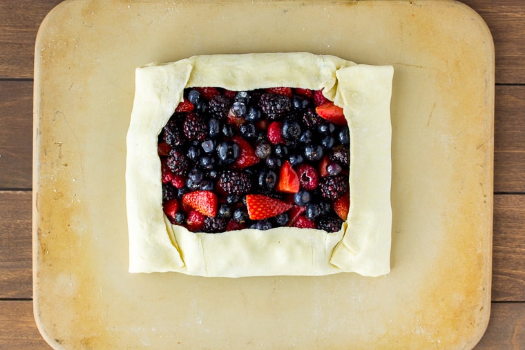 Puff pastry tart folded over mixed berries on a rectangular pizza stone over a wood backdrop