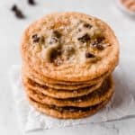 A stack of 6 salted caramel chocolate chip cookies on a white background with chocolate chips around it