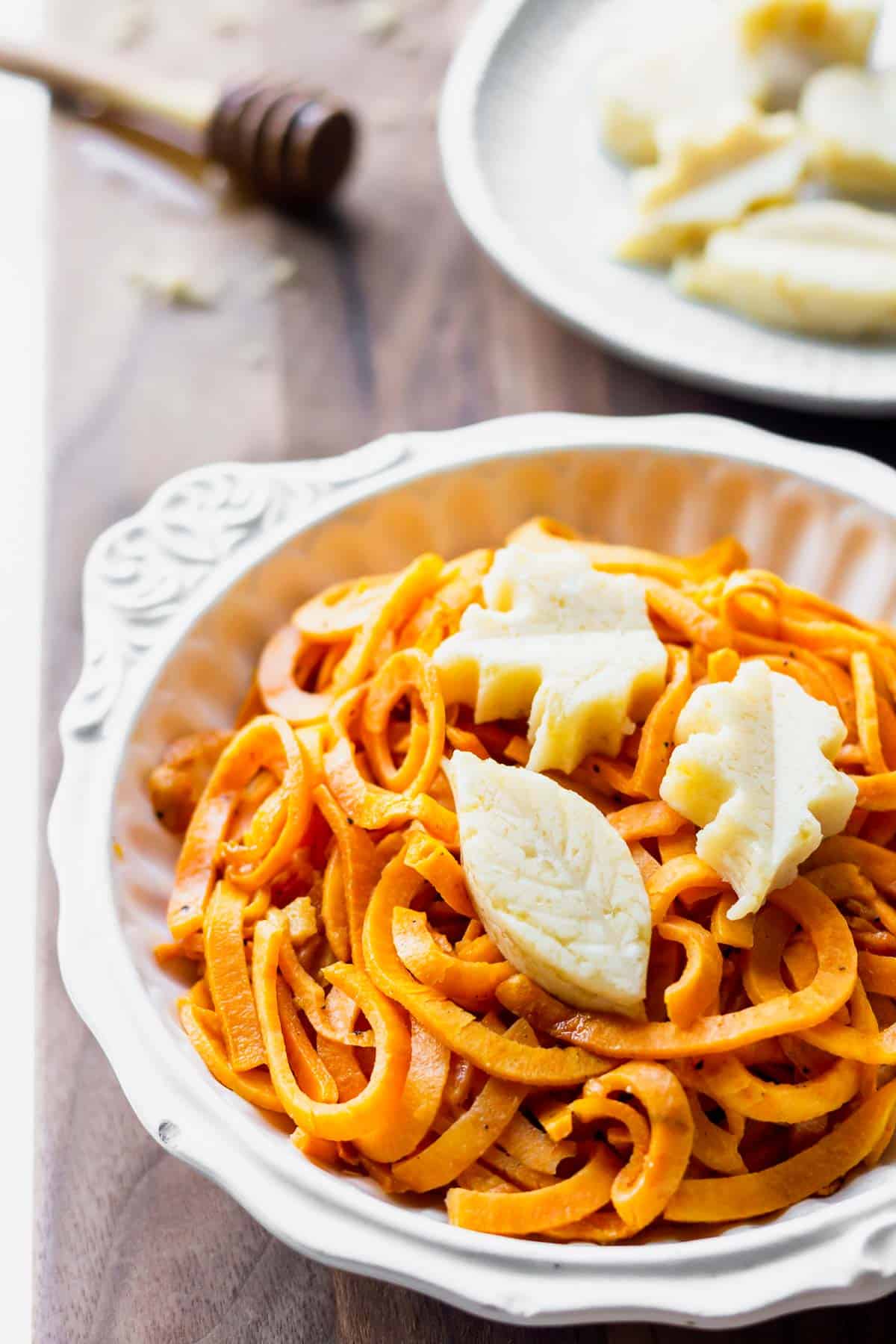 Close up of spiralized sweet potato with brown sugar honey butter on top and a honey dipper and plate of extra butter in the background