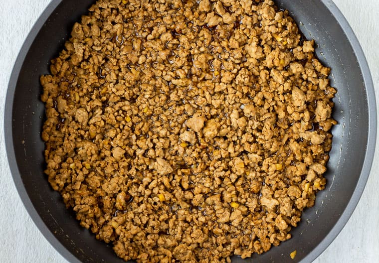 Seasoned browned ground pork crumbles in a black skillet over a white background